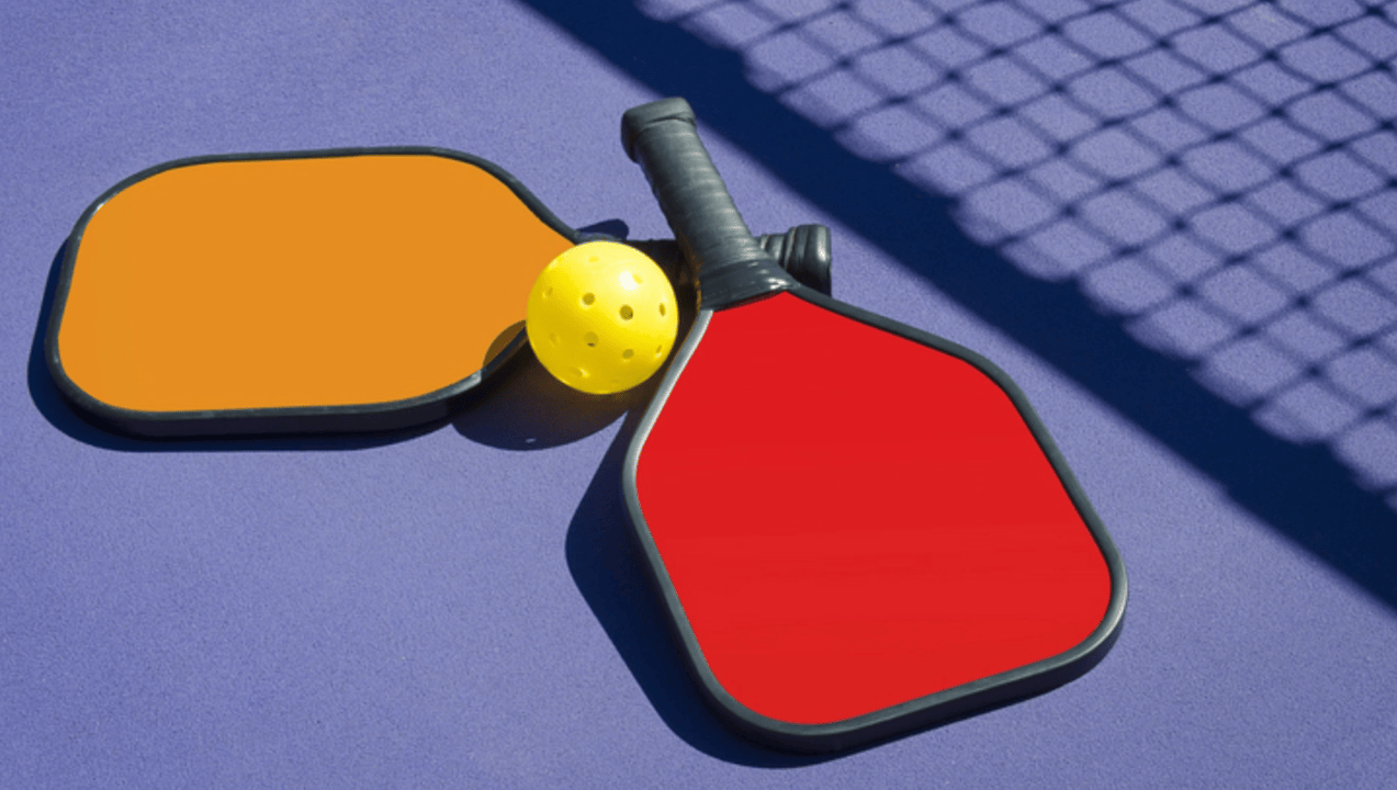 Pickleball paddles and ball in the shadow of a net.