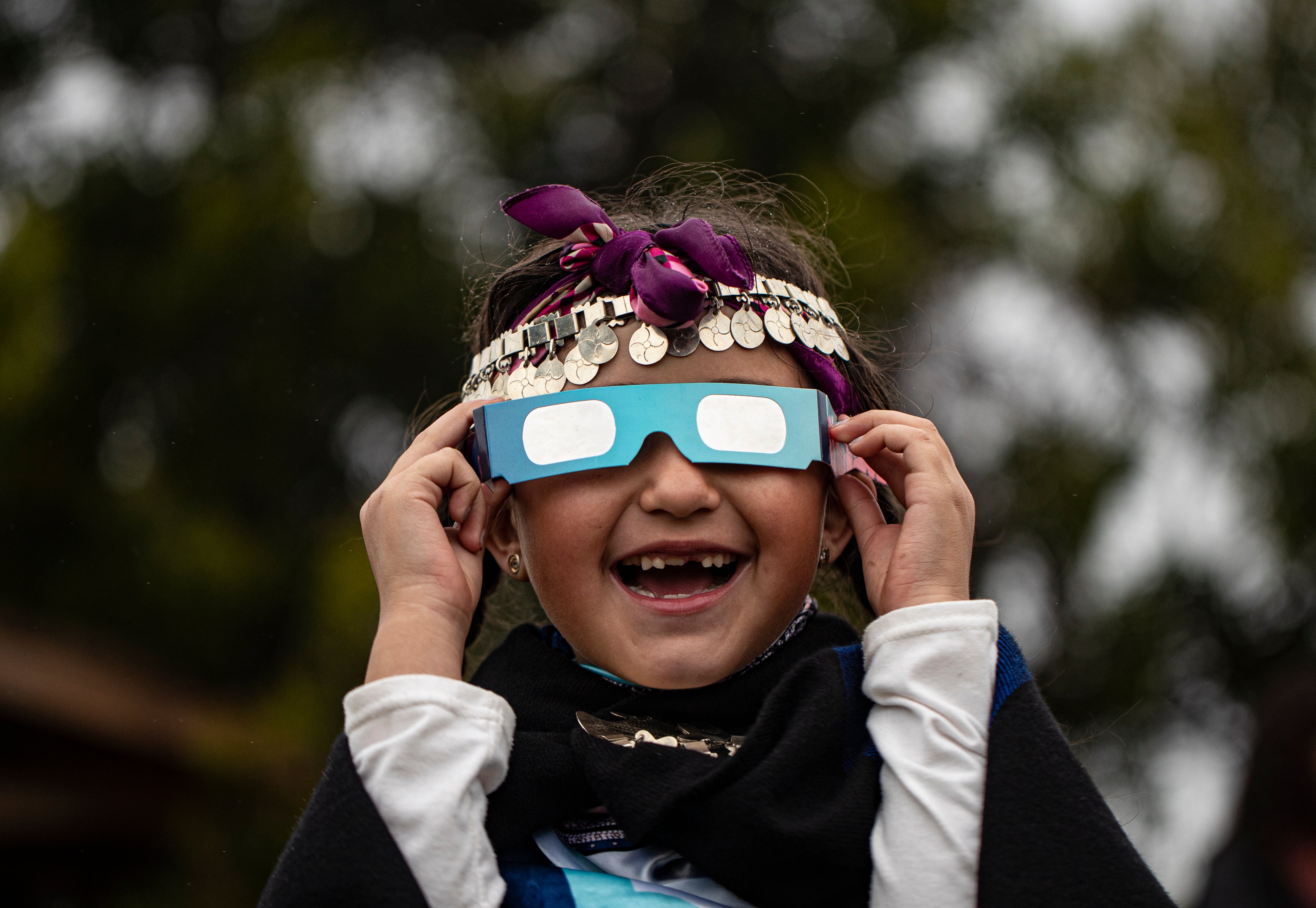 Magdalena Nahuelpan, a Mapuche Indigenous girl, looks at a total solar eclipse using special glasses in Carahue, La Araucania, Chile, Monday, Dec. 14, 2020. (AP Photo/Esteban Felix, File)