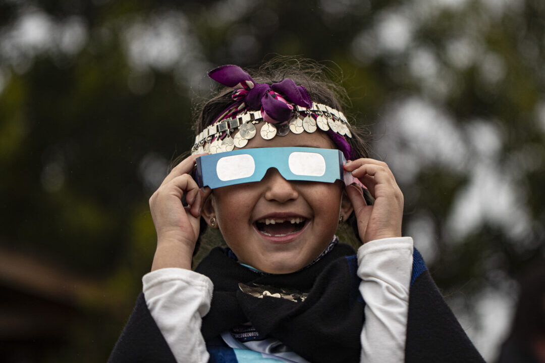 Magdalena Nahuelpan, a Mapuche Indigenous girl, looks at a total solar eclipse using special glasses in Carahue, La Araucania, Chile, Monday, Dec. 14, 2020. (AP Photo/Esteban Felix, File)