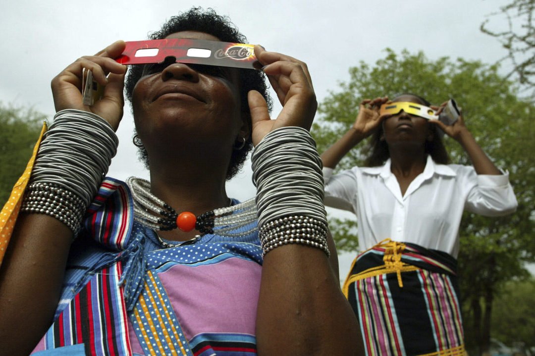 FILE - Lucy Maphiri, left, and Margaret Makuya watch the total solar eclipse over Shingwedzi camp in the Kruger National Park, South Africa, Wednesday, Dec. 4, 2002. (AP Photo/Jon Hrusa, File)