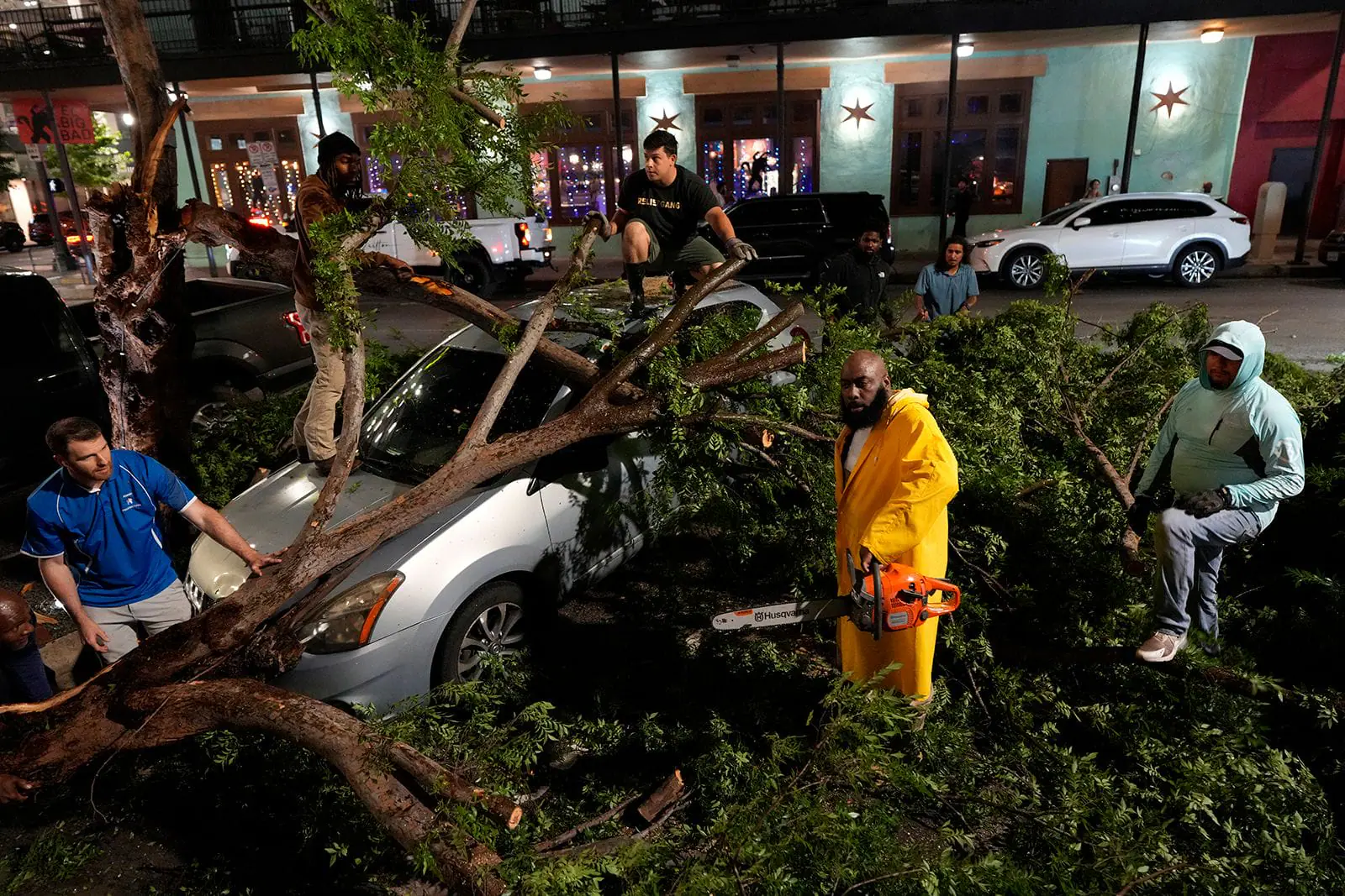 Rapper Trae tha Truth, in yellow, cuts fallen tree limbs on top of a car in the aftermath of a severe thunderstorm that passed through Houston on Thursday.