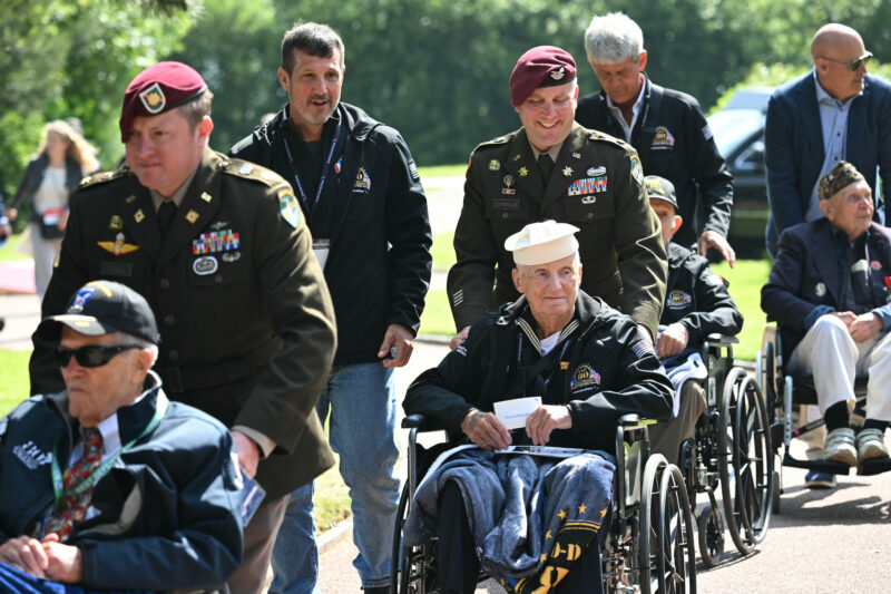 US servicemen escort US WWII veterans in wheelchairs as they arrive for the US ceremony marking the 80th anniversary of the World War II "D-Day" Allied landings in Normandy, at the Normandy American Cemetery and Memorial in Colleville-sur-Mer, which overlooks Omaha Beach in northwestern France, on June 6, 2024. The D-Day ceremonies on June 6 this year mark the 80th anniversary since the launch of 'Operation Overlord', a vast military operation by Allied forces in Normandy, which turned the tide of World War II, eventually leading to the liberation of occupied France and the end of the war against Nazi Germany. (Photo by SAUL LOEB / AFP) (Photo by SAUL LOEB/AFP via Getty Images)