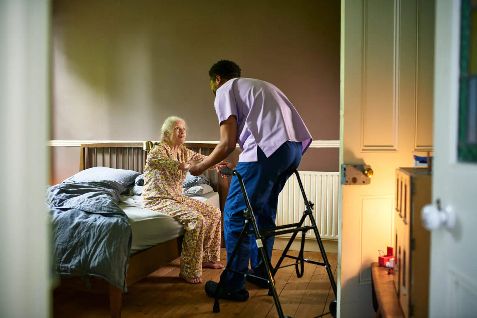 Senior woman smiling and looking up at male carer, holding hands, preparing to stand up. Some nursing home operators in Indiana say they haven't been paid since the state transitioned to managed care on July 1. (Getty Images)