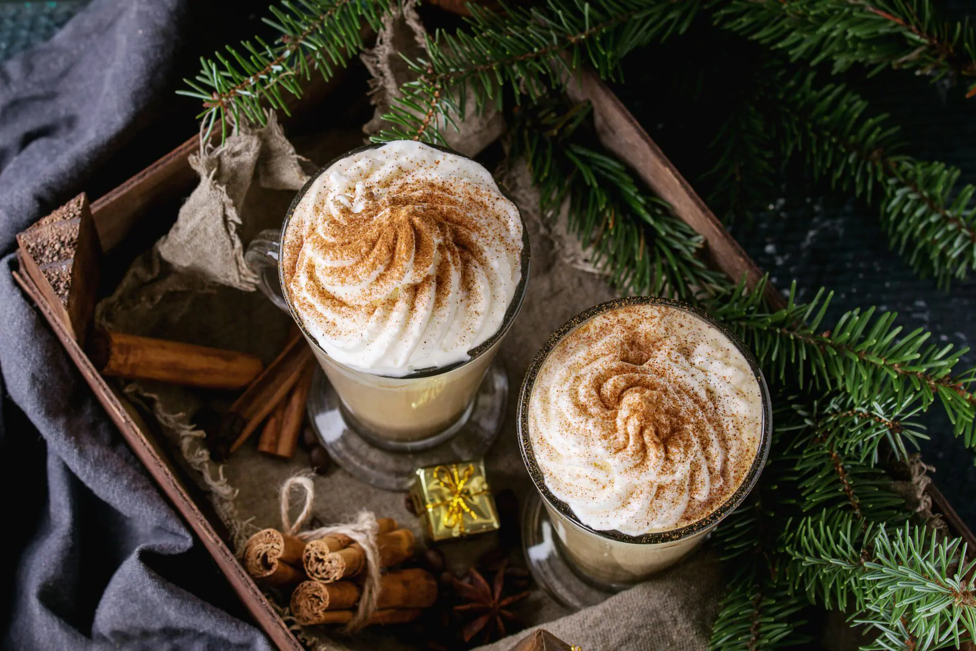 Pumpkin spicy latte with whipped cream and cinnamon in two glasses standing in wooden board with textile and Christmas decoration and fir tree other dark background. Christmas theme, top view. (Photo by: Natasha Breen/REDA&CO/Universal Images Group via Getty Images)