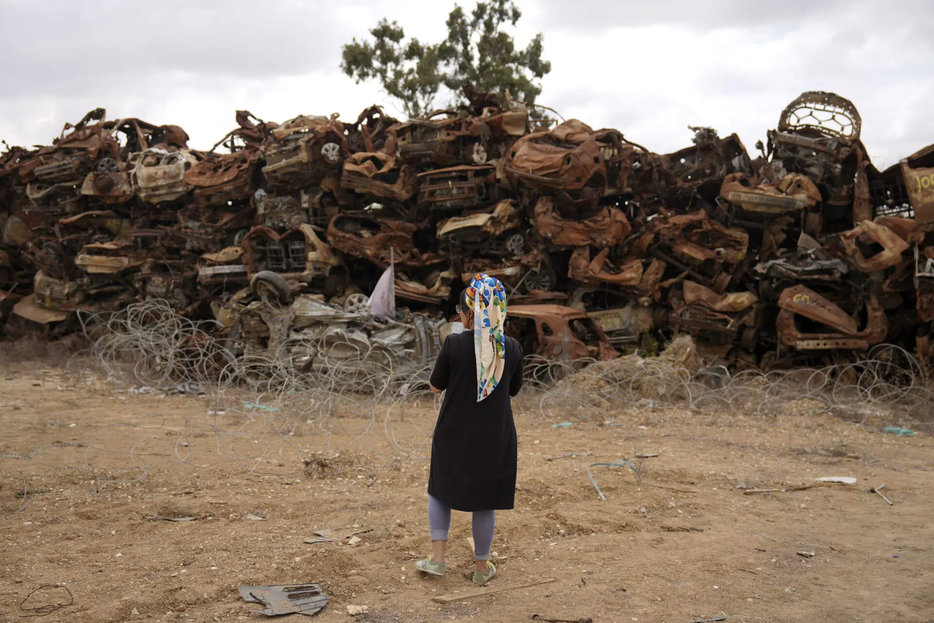 A woman looks at charred vehicles burned in the Oct. 7 cross-border attack by Hamas militants outside the town of Netivot, southern Israel, Monday, Oct. 7, 2024. (AP Photo/Ariel Schalit)