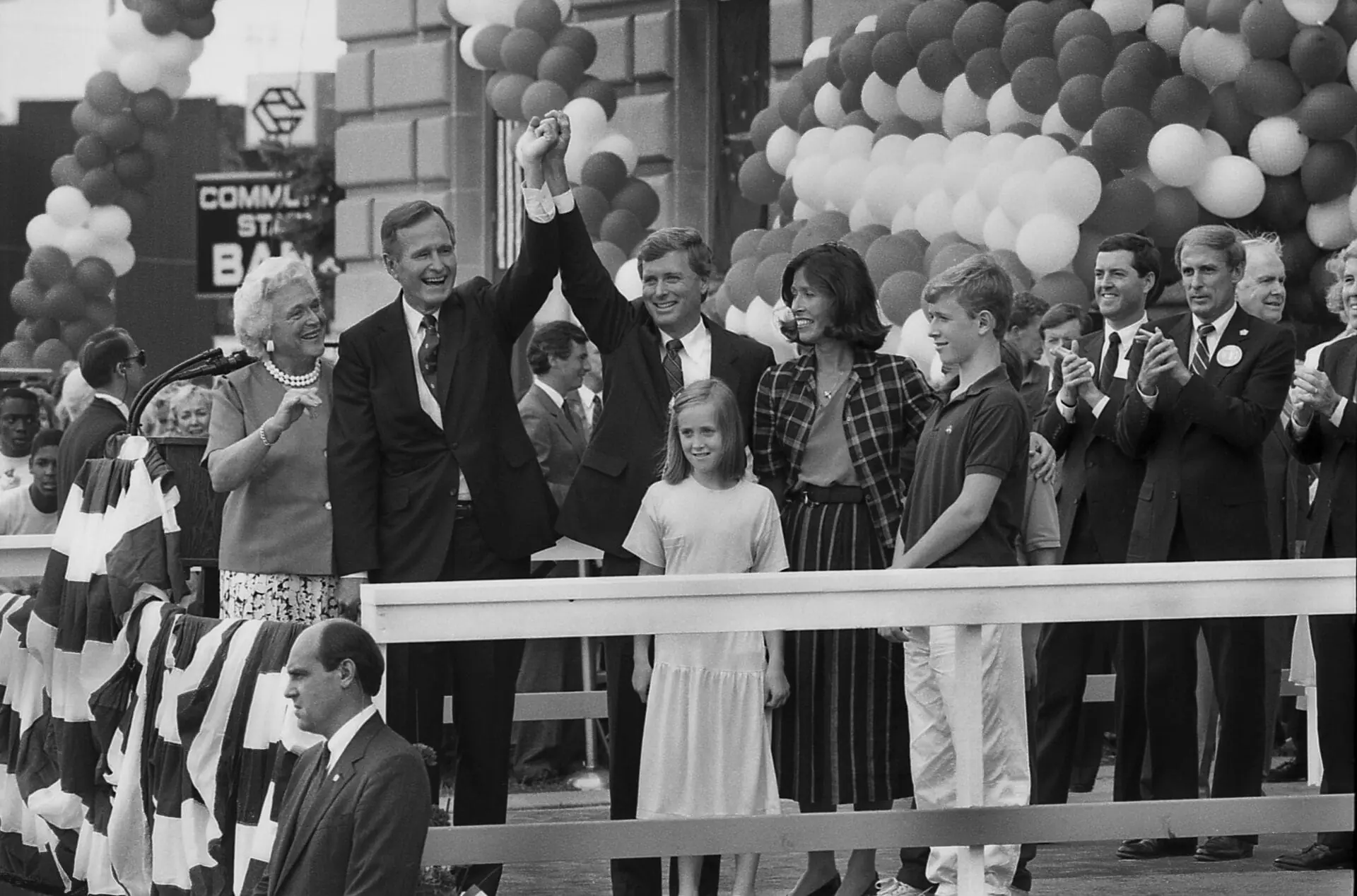 American politician George HW Bush and Dan Quayle raise their hands on a podium during a campaign rally, Huntington, Indiana, August 18, 1988. Among those also on the podium are Bush's wife, Barbara Bush (left), and Marilyn Quayle (in checkered outfit). The event was the first stop after the Bush/Quayle ticket had been nominated at the 1988 Republican National Convention, one day earlier. (Photo by Ed Lallo/Getty Images)