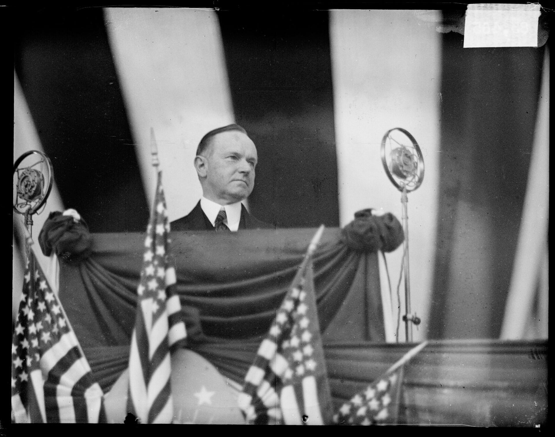 Informal portrait of President Calvin Coolidge standing behind a podium and looking to his left at a dedication ceremony for Wicker Park, Lake County, Indiana, June 14, 1927. Coolidge dedicated Wicker Park as a memorial to soldiers who hailed from Lake County. (Photo by Chicago Sun-Times/Chicago Daily News collection/Chicago History Museum/Getty Images)