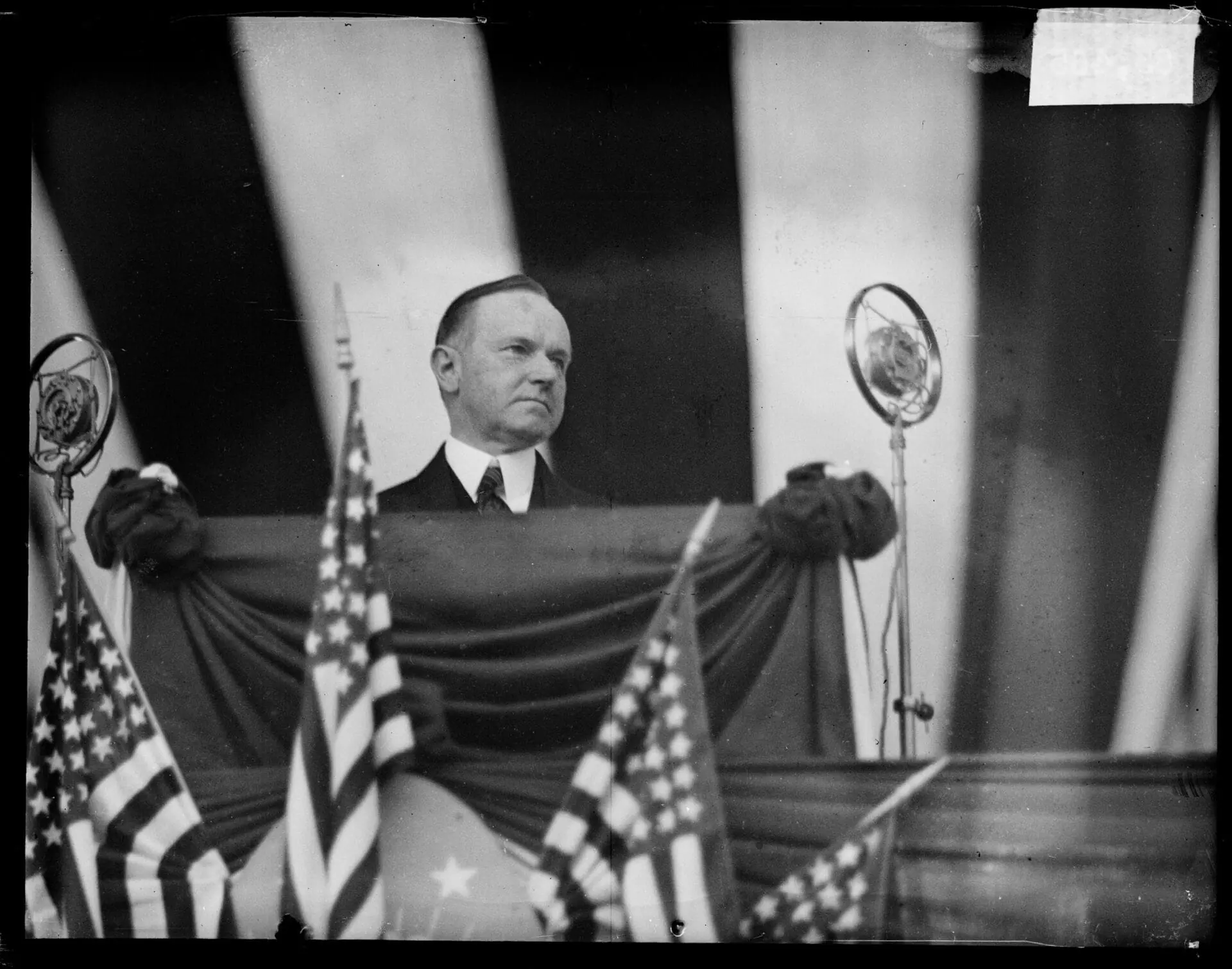 Informal portrait of President Calvin Coolidge standing behind a podium and looking to his left at a dedication ceremony for Wicker Park, Lake County, Indiana, June 14, 1927. Coolidge dedicated Wicker Park as a memorial to soldiers who hailed from Lake County. (Photo by Chicago Sun-Times/Chicago Daily News collection/Chicago History Museum/Getty Images)