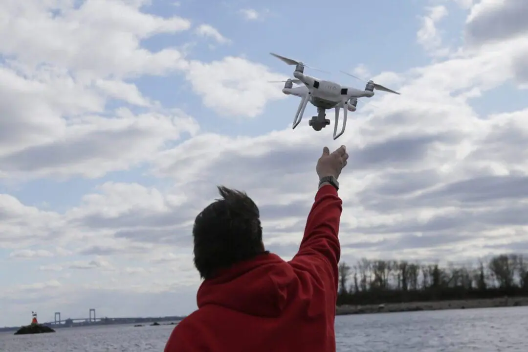 FILE - In this April 29, 2018, file photo, a drone operator helps to retrieve a drone after photographing over Hart Island in New York. Experts say if you’re trying to determine whether that’s a drone in the sky, you should look at how it moves and listen to the sounds it makes. Only drones can make tight turns and move sideways, and they're likely to make a high-pitched humming noise. (AP Photo/Seth Wenig, File)