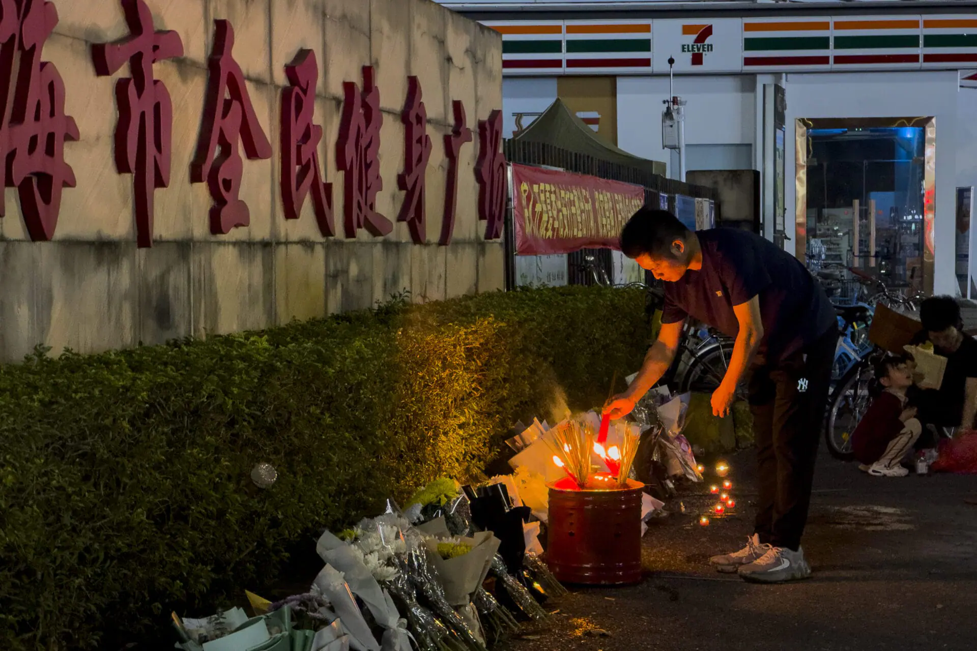 A man lights a candle near flowers placed outside the 